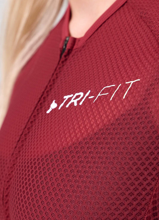 Close-up of TRI-FIT logo printed on the chest of the VANGUARD tri-suit in wine red, showing textured breathable fabric